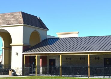 A modern building with a dark metal roof under a clear blue sky.