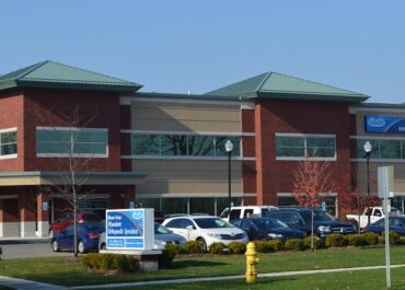 View of a medical center building with parked cars and a sign.
